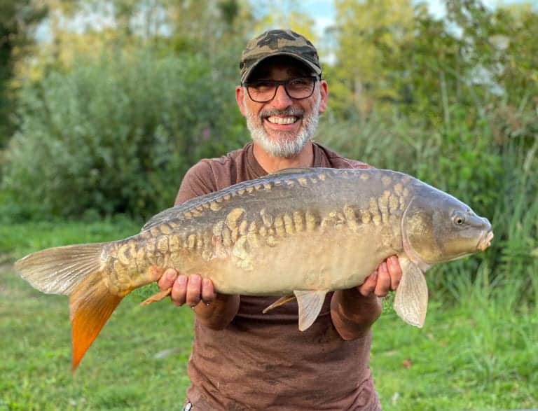 Smiling man holding large fish outdoors.