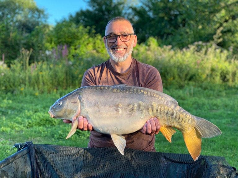 Man holding large fish outdoors in garden.