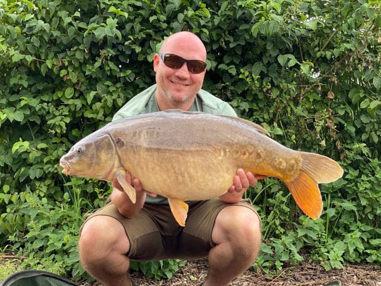 Smiling man holding large carp fish outdoors.