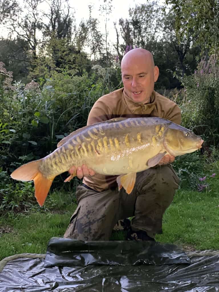 Man holding large fish in garden setting.