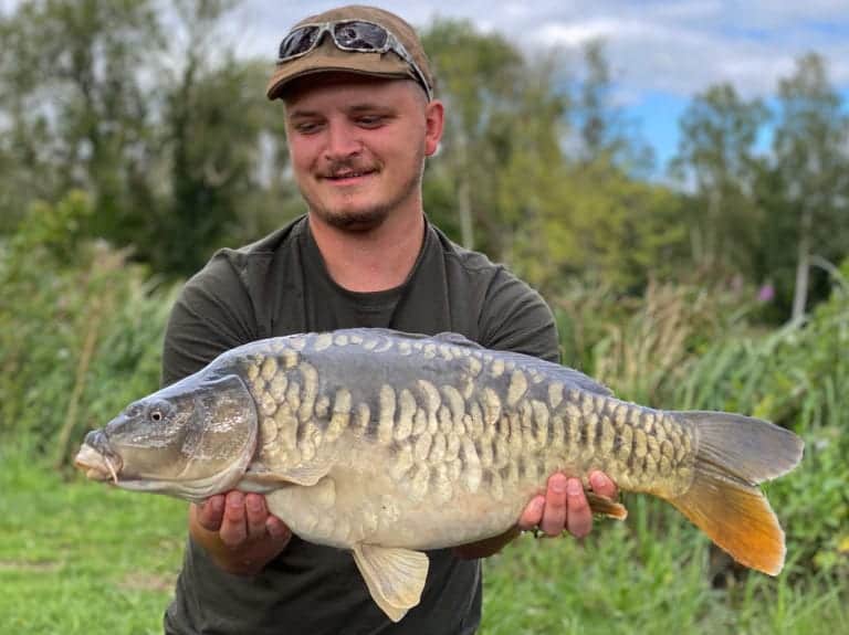 Person holding a large mirror carp outdoors.
