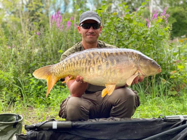 Man proudly holding large carp fish outdoors.