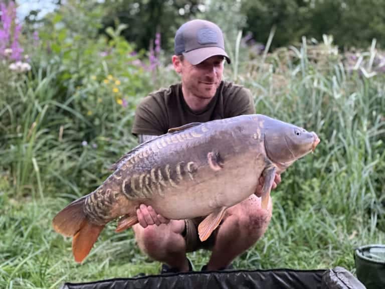 Man holding large carp by riverbank