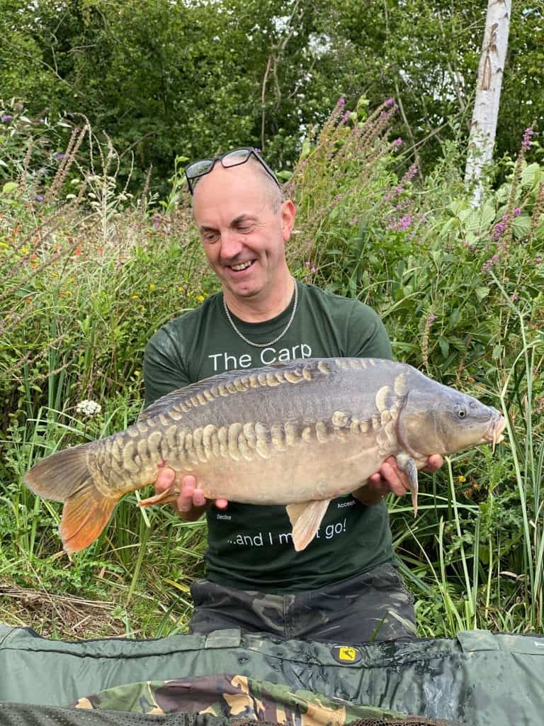 Man smiling, holding large carp, outdoor setting.