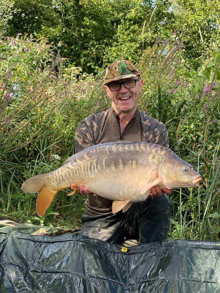 Angler holding large carp by the riverbank.