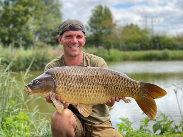Person holding a carp by the riverbank.