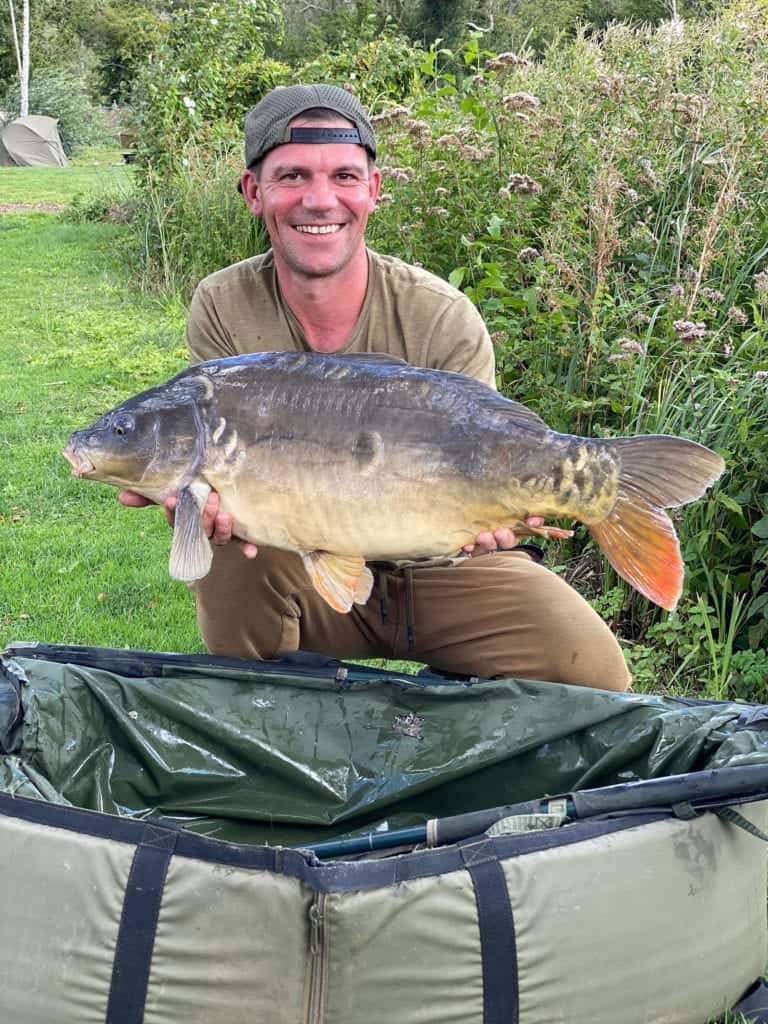Angler holds large carp fish by lake.