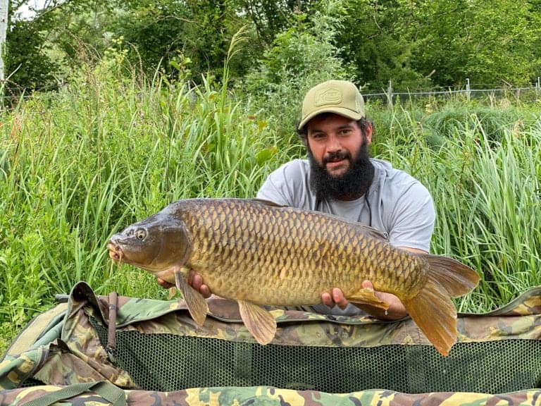 Man holding large fish in grassy area.