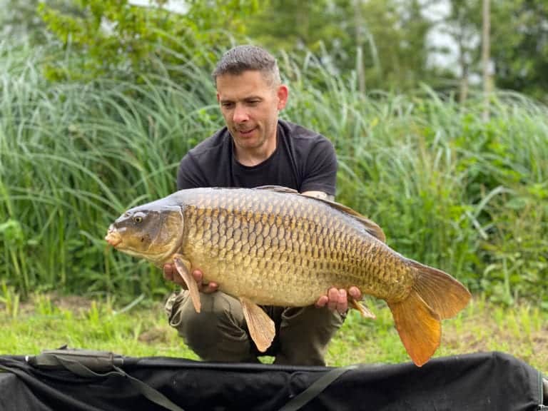 Man holding large fish on lakeside.