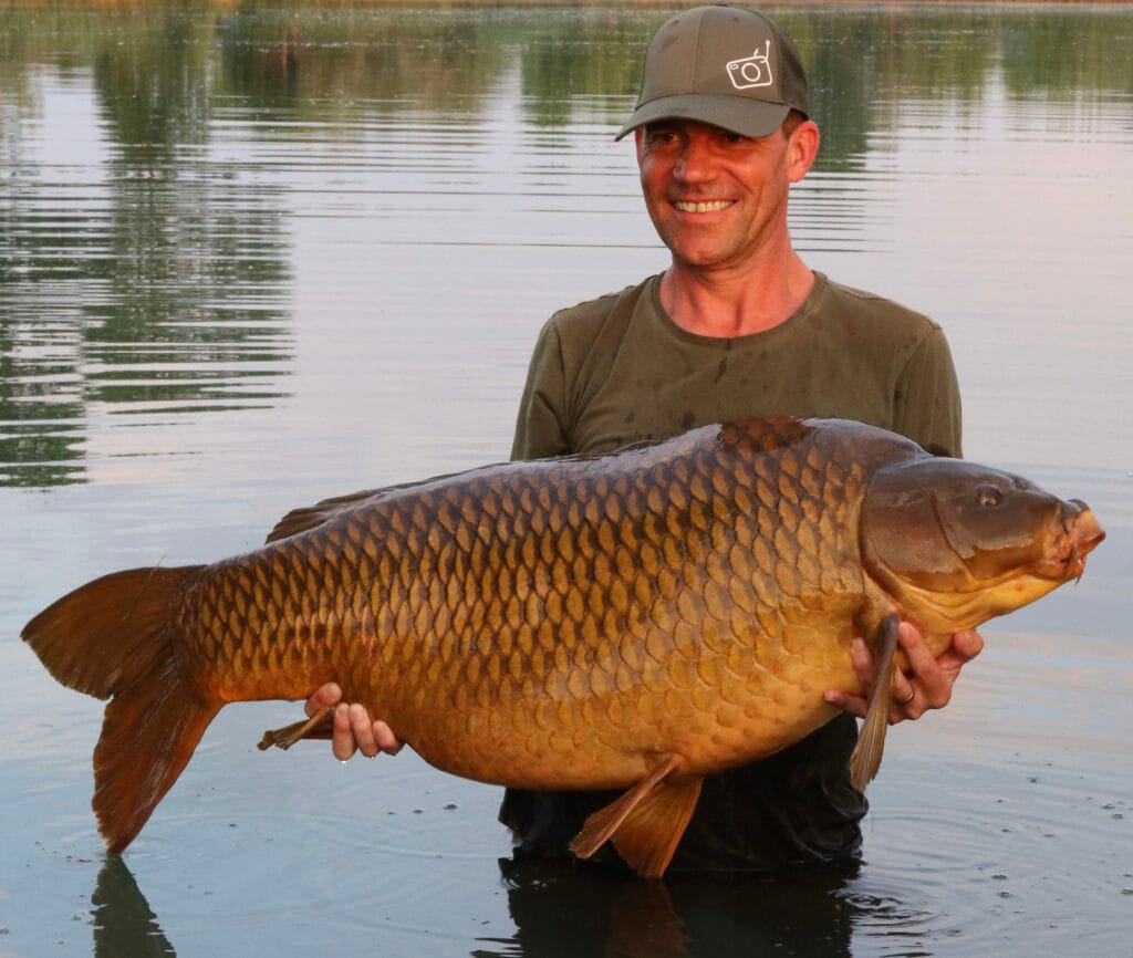 Smiling angler holds large carp in water