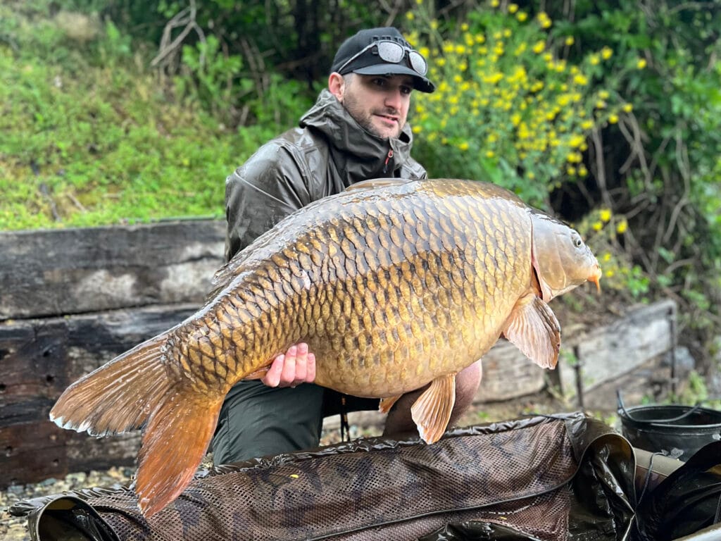 Person holding a large carp near a lake.