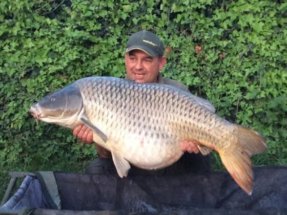 Person holding large fish, leafy background.