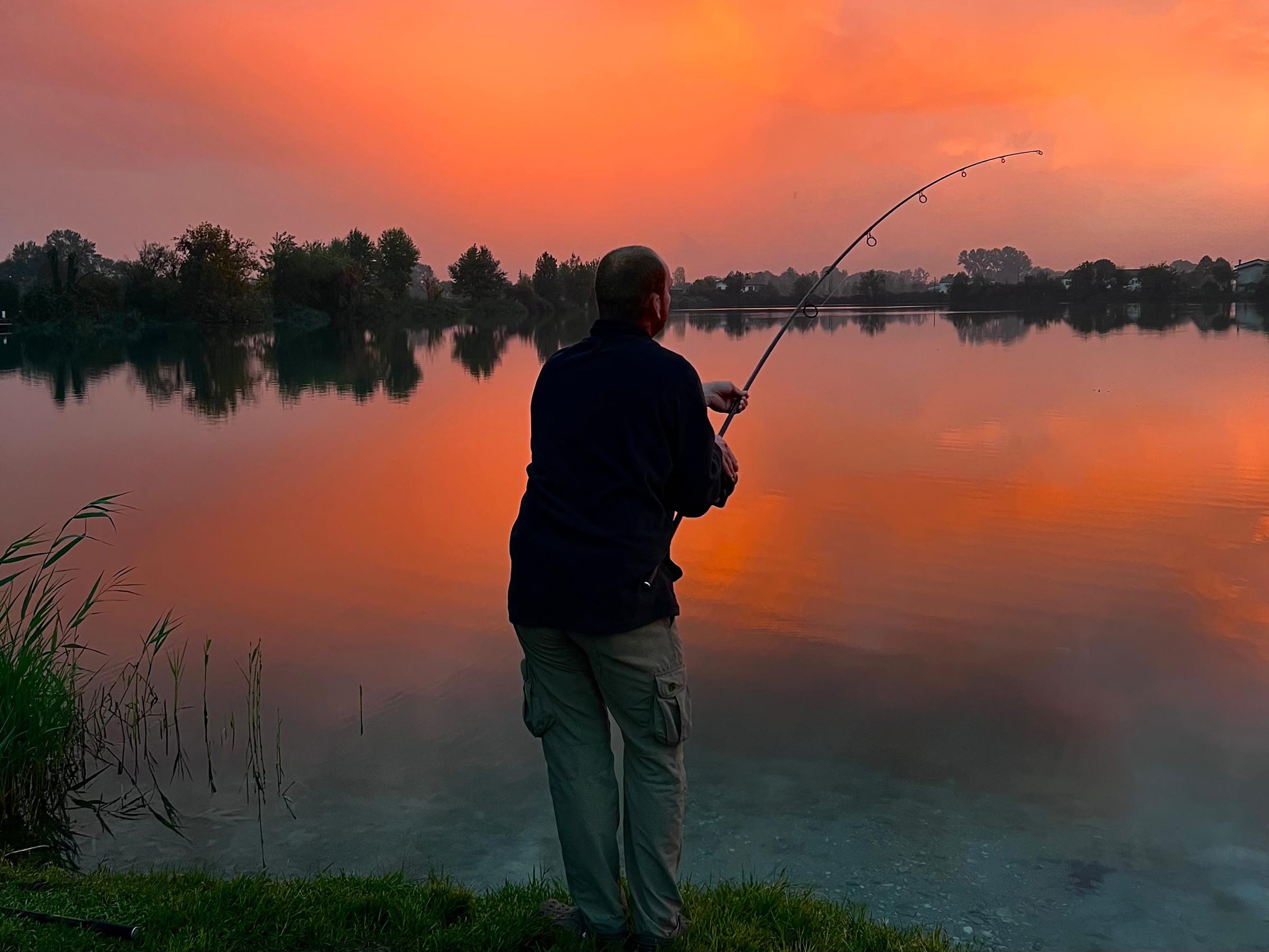 Person fishing at lake during vibrant sunset