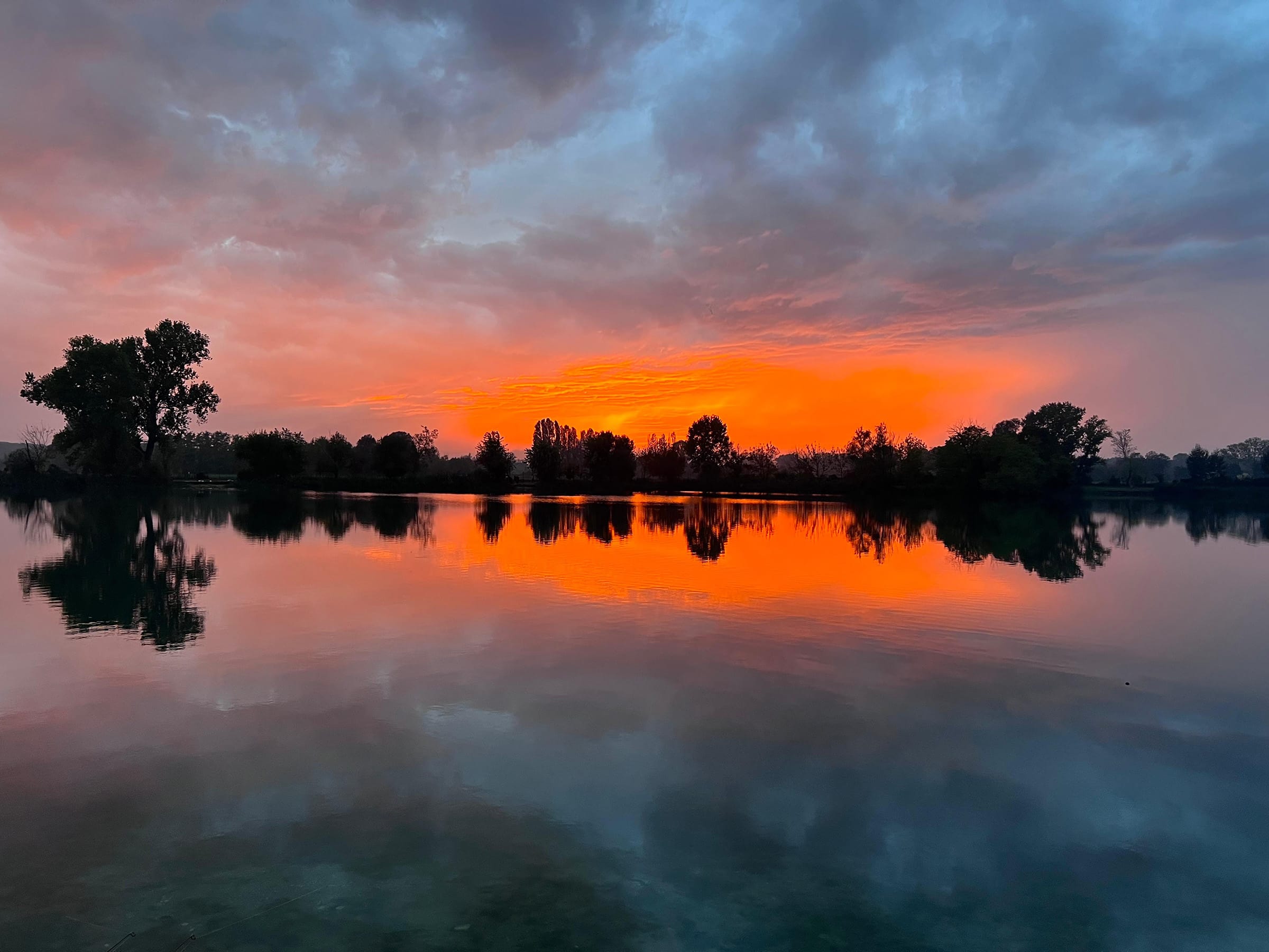 Sunset reflecting on lake with trees silhouetted.